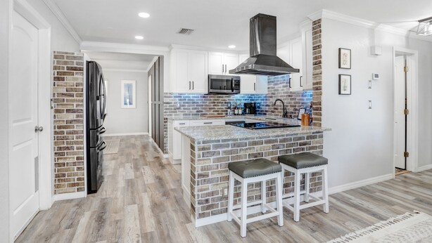 A modern kitchen with a brick backsplash, stainless steel appliances, and a central island with bar stools. - Golf and Pool Vacation Home!
 (St. Petersburg)