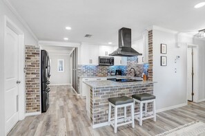 A modern kitchen with a brick backsplash, stainless steel appliances, and a central island with bar stools. - Golf and Pool Vacation Home!
(St. Petersburg)