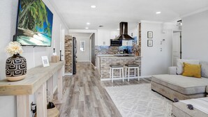 A modern kitchen with a brick backsplash, a central island with stools, and a large flat-screen TV mounted on the wall. - Golf and Pool Vacation Home!
 (St. Petersburg)