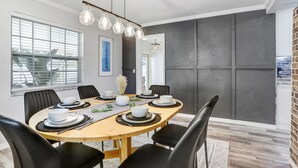 Un coin repas avec une table ronde dressée pour six personnes, des chaises noires et un lustre moderne.