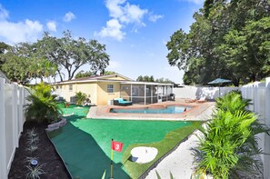 A backyard with a swimming pool, a covered patio, and a lawn. - Golf and Pool Vacation Home!
 (St. Petersburg)
