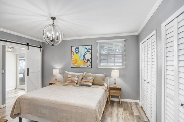 A bedroom with a bed, bedside lamps, a ceiling light, a window with blinds, and a door with a sliding mechanism. - Golf and Pool Vacation Home!
(St. Petersburg)