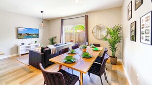 A dining area with a wooden table set for four, surrounded by wicker chairs. There is a sofa and a white cabinet with a television on the wall. - Free Parking | Prime Location Townhouse (Miami)
