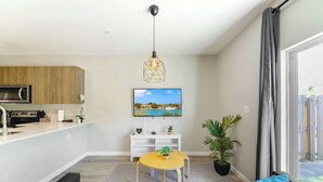 A modern living room with a sofa, a small yellow table, a TV, and a kitchen area with wooden cabinets and a microwave. - Free Parking | Prime Location Townhouse (Miami)