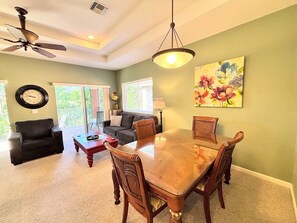 A dining area with a wooden table and chairs, a ceiling fan, and a painting on the wall. - Right Direction Rentals 1 Bedroom Villa 8271 (Port St. Lucie)