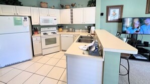 Een compacte keuken met witte kastjes, een magnetron, oven, en een klein eiland met een spoelbak.