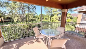 Een overdekt terras met een ronde glazen tafel en vier stoelen, omringd door een metalen hekwerk.