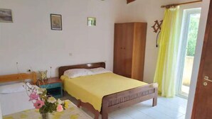 Une chambre à coucher avec un lit en bois, une table de chevet, une table recouverte d’une nappe jaune et une fenêtre avec des rideaux jaunes.