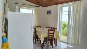 Un coin repas avec une table dressée pour quatre personnes, des chaises en bois, un réfrigérateur blanc et une fenêtre avec des rideaux.