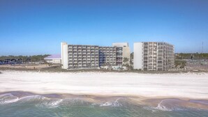 Ein Hotel direkt am Strand mit mehreren Etagen und Balkonen, gelegen an einem Sandstrand, im Vordergrund sind Wellen zu sehen.