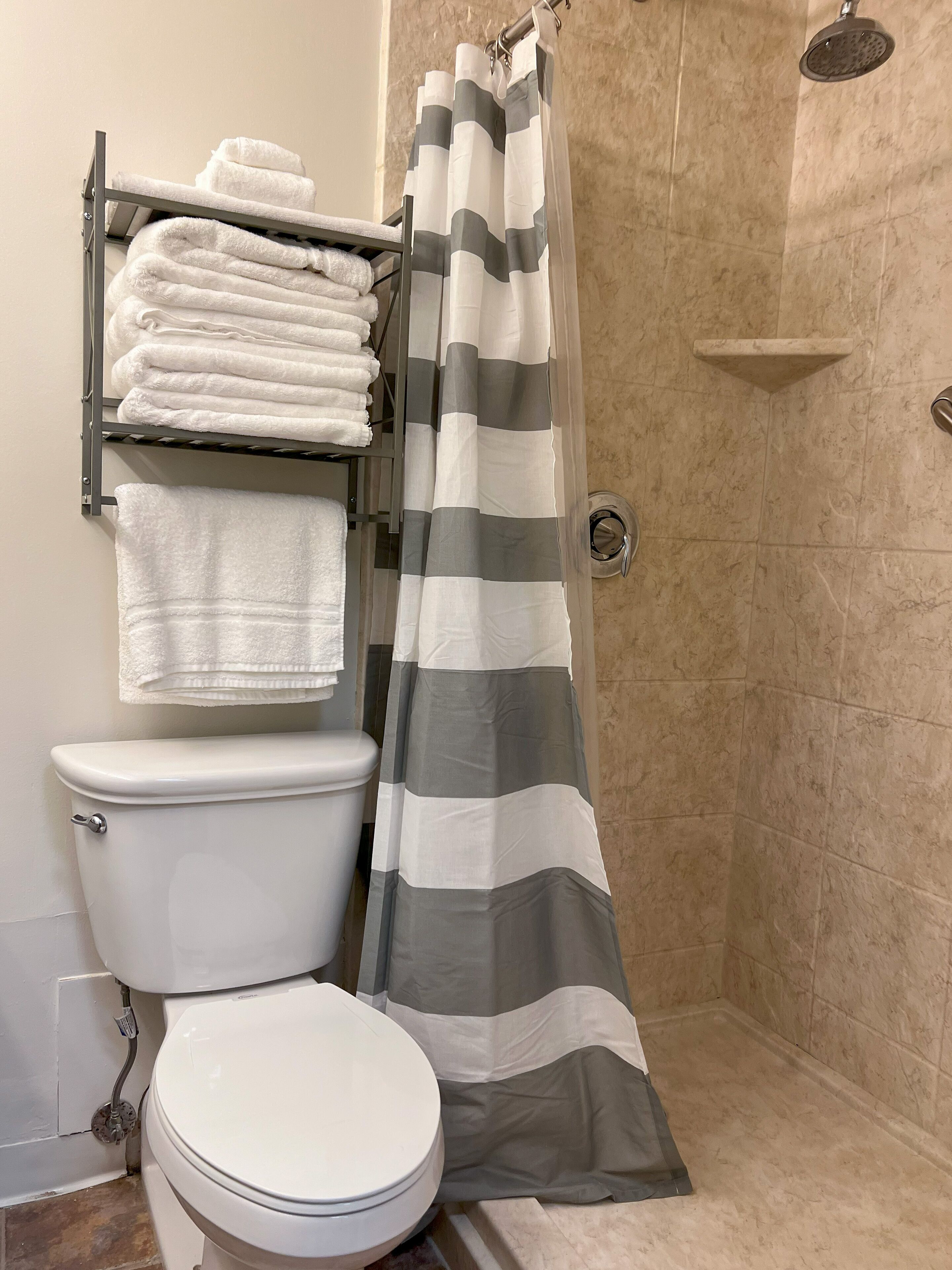 A bathroom with a toilet, a towel rack with folded towels, a shower curtain, and a showerhead.
