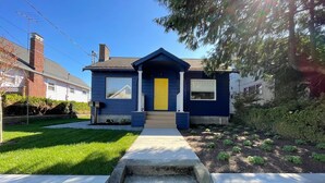 A residential house with a blue exterior, a yellow front door, and a front yard with a concrete pathway leading to the entrance. - Skyline Blue House in Greenwood (Seattle)