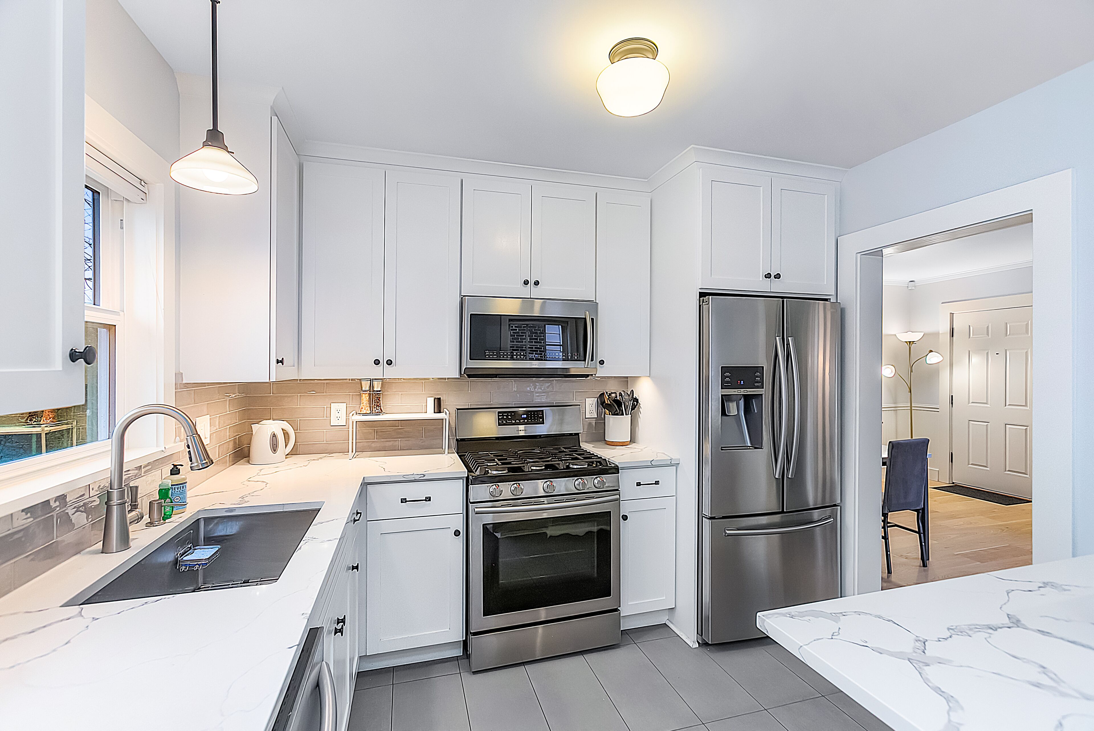 A modern kitchen with white cabinets, stainless steel appliances, and a marble countertop.