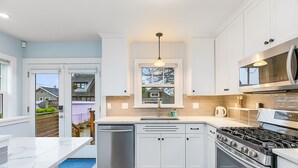 A modern kitchen with white cabinets, a stainless steel dishwasher, a gas stove, and a microwave. - Skyline Blue House in Greenwood (Seattle)