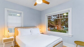 A bedroom with a bed, a nightstand, a window with a view of trees, and a ceiling fan. - Skyline Blue House in Greenwood (Seattle)