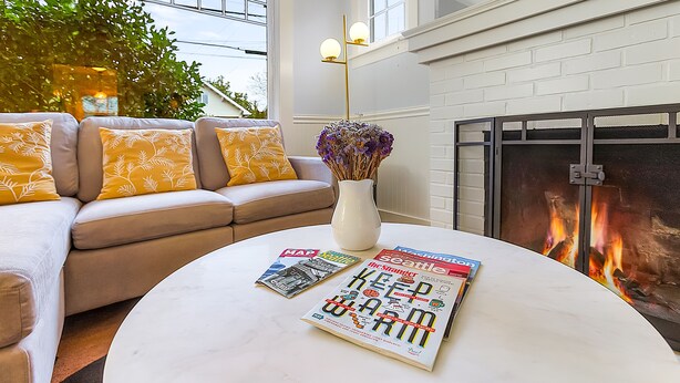 A cozy living room with a sofa, a round coffee table with magazines, a vase with flowers, and a fireplace. - Skyline Blue House in Greenwood (Seattle)