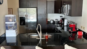 A modern kitchen with dark cabinetry, a stainless steel refrigerator, a sink, and a coffee machine. - Oceanfront Condo with stunning pool and oversized balcony. (Jacó)