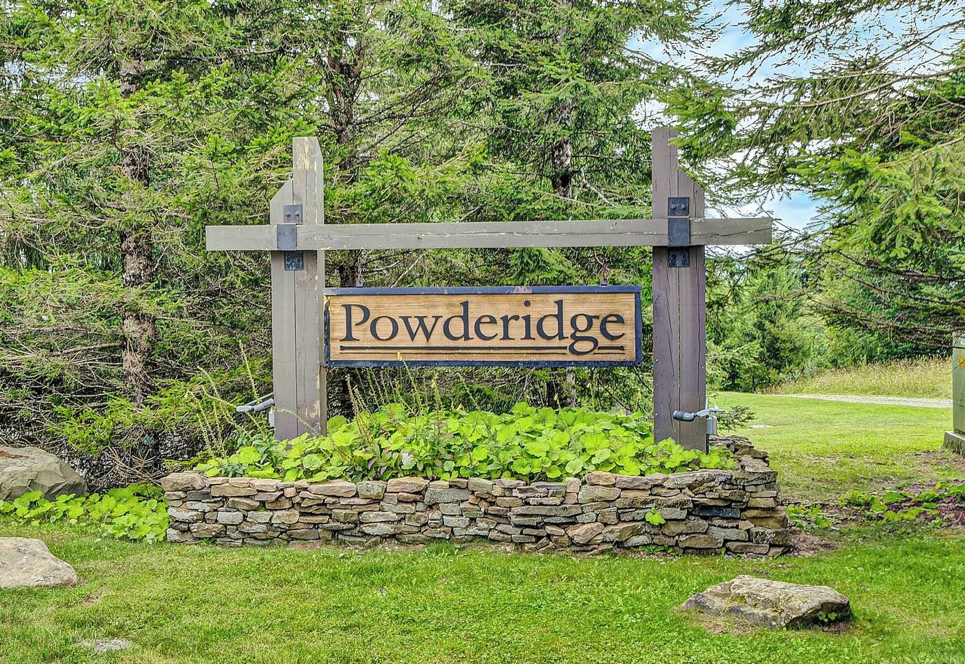 Placa de madeira com o nome 'Powderidge' em um jardim de pedra.