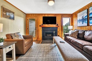 Un salon chaleureux avec une cheminée, des murs en bois et deux canapés en cuir.