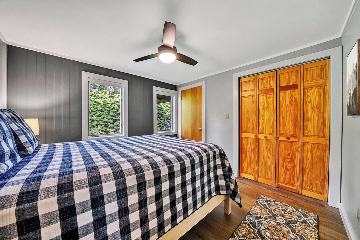 Een slaapkamer met een bed, een plafondventilator, een raam en een houten garderobe.