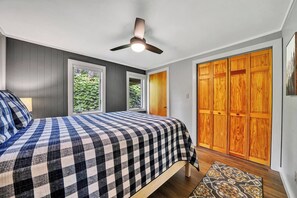 Une chambre à coucher avec un lit, un ventilateur de plafond, une fenêtre et une armoire en bois.