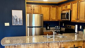 A modern kitchen with wooden cabinets, stainless steel appliances, granite countertops, and bar stools. - 8 Powderidge, Snowshoe, WV - Slopeside Sanctuary (Snowshoe)