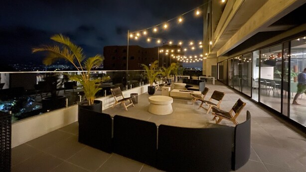 A rooftop terrace with string lights, seating, and a view of the city at night.