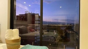 A room with a large window overlooking a cityscape at dusk.