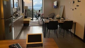 Una cocina moderna con comedor, una laptop sobre la mesa y vista de la ciudad a través de la puerta de vidrio.