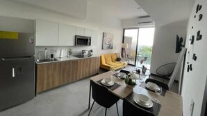 Una cocina moderna con microondas integrado, una zona de comedor con mesa para dos, y un sofá amarillo en la sala.