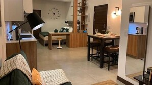 Un espacio habitable compacto con kitchenette, comedor y zona de estar con sofá y mesa de centro.