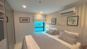 A bedroom with a large bed, a window with blinds, a wall-mounted air conditioner, and framed pictures on the wall. - PRIME LOK- SP FLAT JARDINS I (São Paulo)