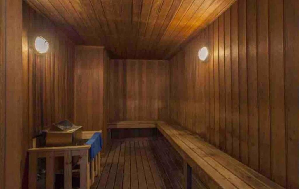 Eine Holzsauna mit Bänken und einem Tisch, ausgestattet mit schrägverlaufender Decke und wandmontierten Leuchten.
