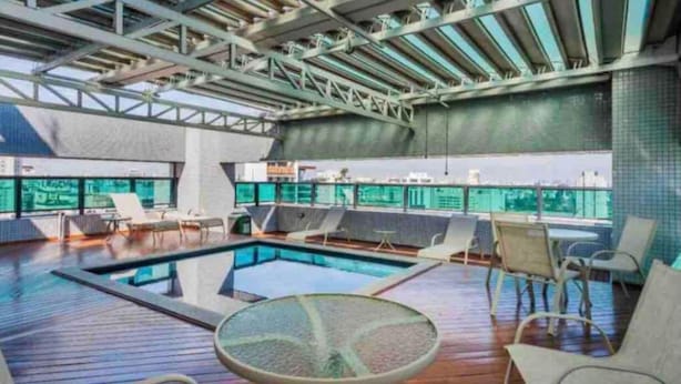 A rooftop pool area with a glass balustrade, lounge chairs, and a view of the cityscape. - PRIME LOK- SP FLAT JARDINS I (São Paulo)