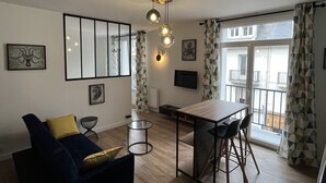 Ein modernes Wohnzimmer mit Sofa, Couchtisch, Fernseher und einem Balkon mit gemusterten Vorhängen.