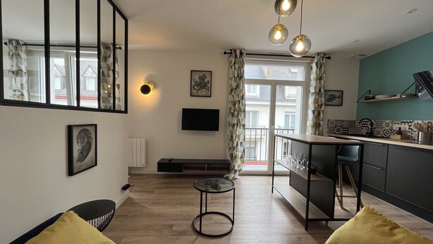 Ein modernes Wohnzimmer mit einer Couch, einem Couchtisch und einem Fernseher. Es gibt eine Küchenzeile mit einer Arbeitsplatte und einem Spülbecken.