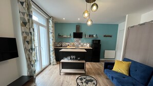 Ein modernes Wohnzimmer mit einem blauen Sofa, einem Couchtisch mit Weltkarten-Design und einer Küchenzeile, die eine Mikrowelle und dekorative Fliesen aufweist.