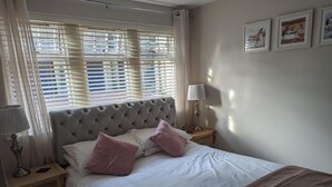 A neatly made bed with a tufted headboard, two pink pillows, and a white comforter. There is a wooden nightstand with a lamp and a clock. - Stunning 1-bed Apartment in Rothbury, Morpeth (Morpeth)