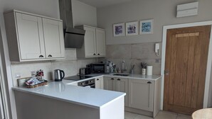 A modern kitchen with a central island, white cabinets, a microwave, toaster, and a sink. There are three framed pictures on the wall and a wooden door. - Stunning 1-bed Apartment in Rothbury, Morpeth (Morpeth)