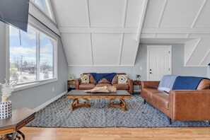 A loft-style room with a sloped ceiling, a brown leather sofa, a wooden coffee table, and a patterned rug.