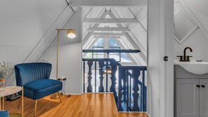 A modern loft bedroom with a sloped ceiling, a blue chair, a round table, and a view of the outdoors.