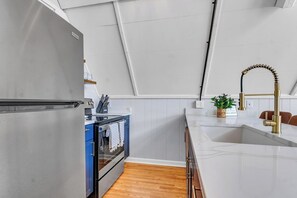Una cocina con un refrigerador de acero inoxidable, un horno empotrado, un lavamanos con grifo dorado y piso de madera.