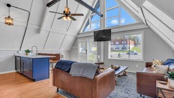 Relax in this open-plan living space with a high ceiling and skylight, featuring a central seating area, dining table, and kitchen with modern cabinetry.