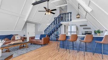 Un loft amplio con techo alto, área de cocina, zona de estar con sofá y sillas, y una escalera.