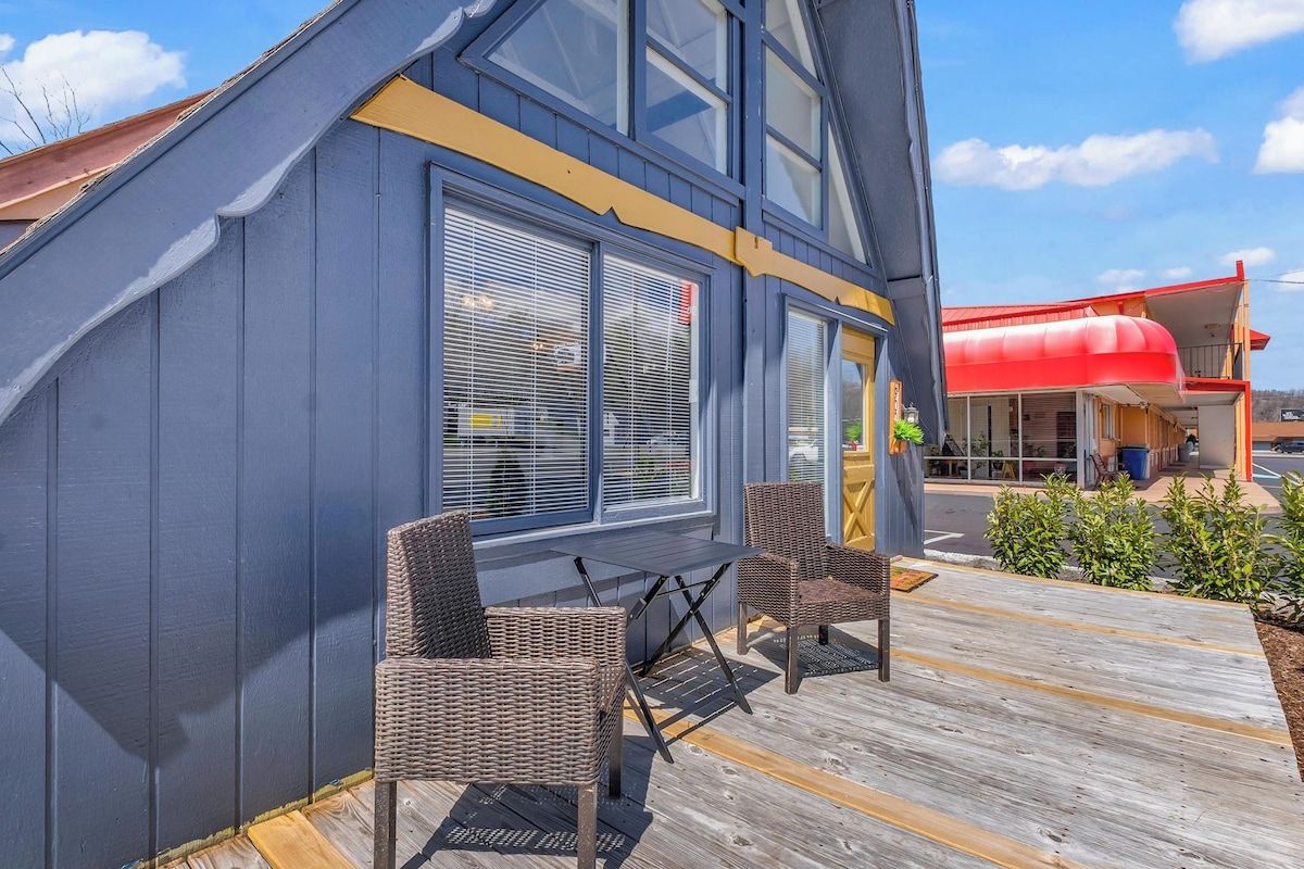 A modern building with a sloped roof, large windows, and a wooden deck with wicker chairs.