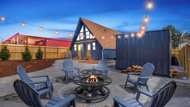 A patio area with a fire pit, outdoor seating, and a house in the background.