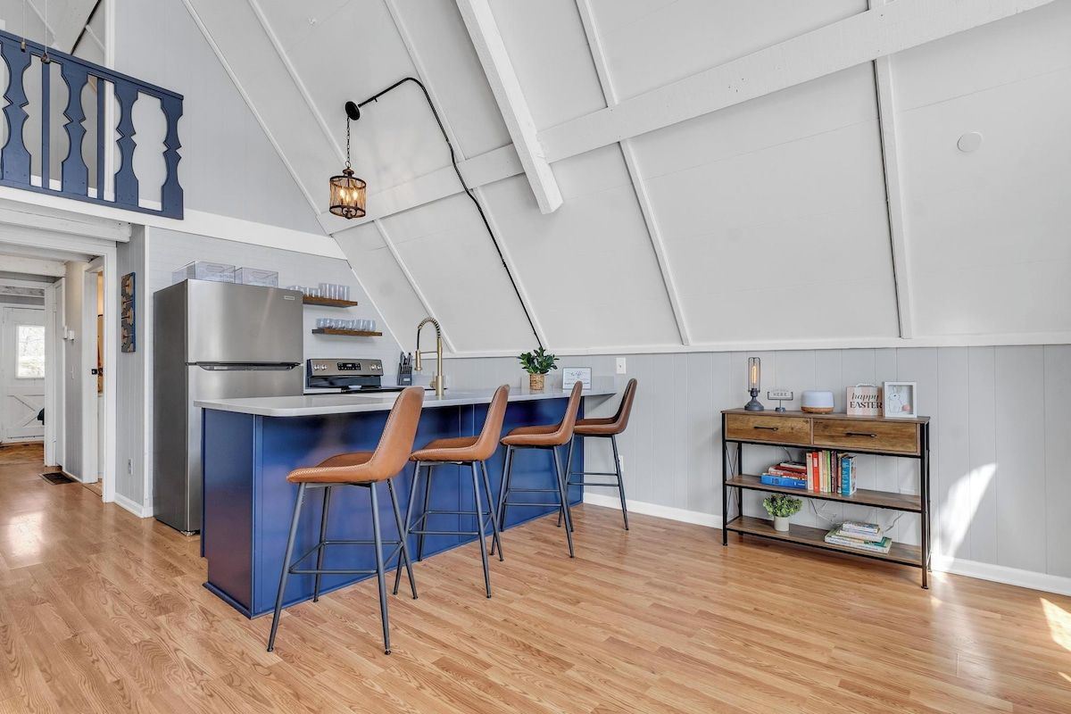 A modern kitchen with a central island, bar stools, a built-in refrigerator, and a pendant light.