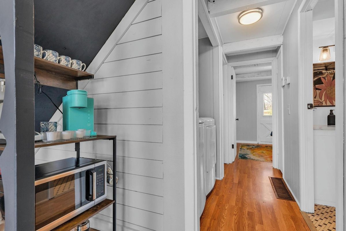A hallway with wooden flooring, a microwave, and a shelf with cups and a water dispenser.