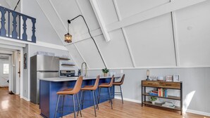 A modern kitchen with a central island, bar stools, a built-in refrigerator, and a wooden bookshelf.