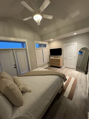 A bedroom with a bed, a ceiling fan, a TV, and a door. - 1 min. golf cart ride to the beach! Family-sized house w/ deck & fenced backyard (Panama City Beach)